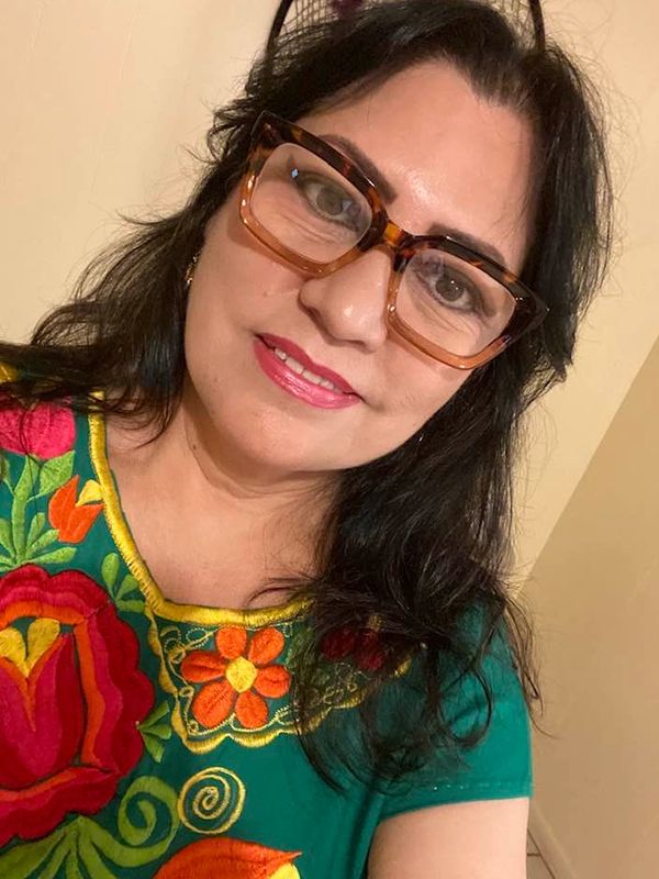 Mujer con gafas grandes y blusa bordada de flores.