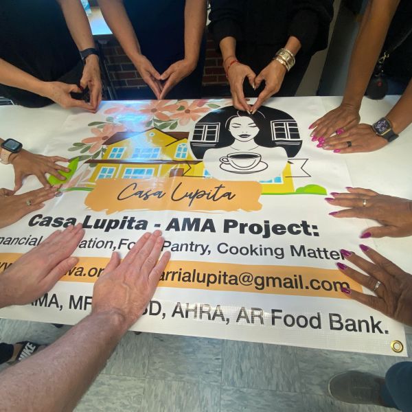 Manos alrededor de una pancarta del proyecto Casa Lupita.