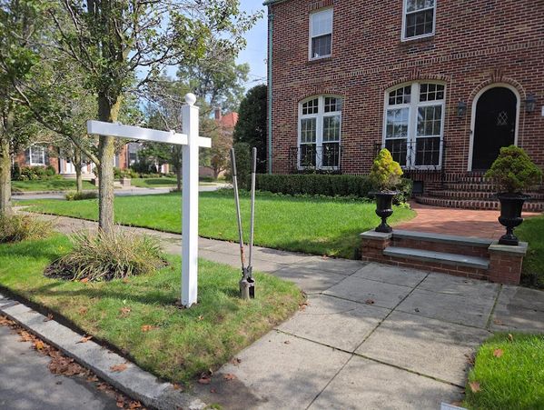 Empty white real estate signpost on green lawn beside brick house entrance.