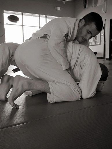 Two men practicing Brazilian Jiu-Jitsu grappling on mats in a training gym.