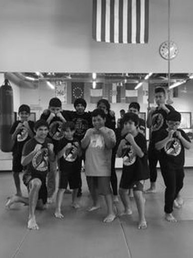 Young martial arts students in fighting stances pose for a group photo in a gym.