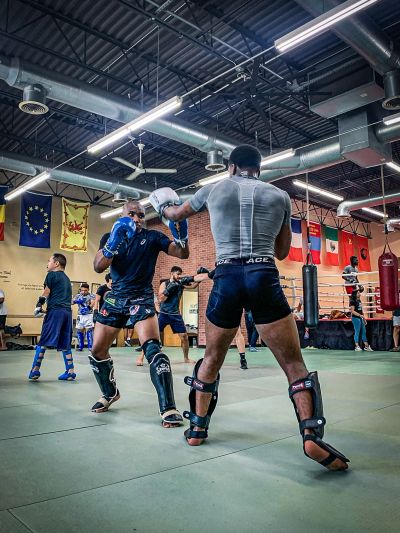 Two men sparring in a gym with others training in the background.