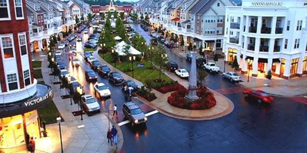 A lively urban street with parked cars and shops at dusk.