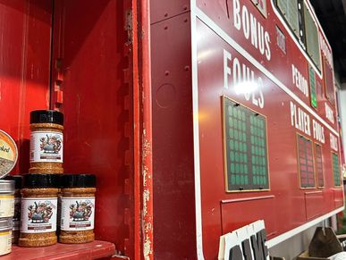 Spicy seasoning jars on a red shelf near a scoreboard.
