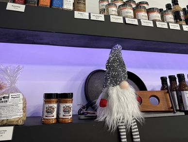 A decorative gnome with a sparkly hat on a kitchen shelf with spices.