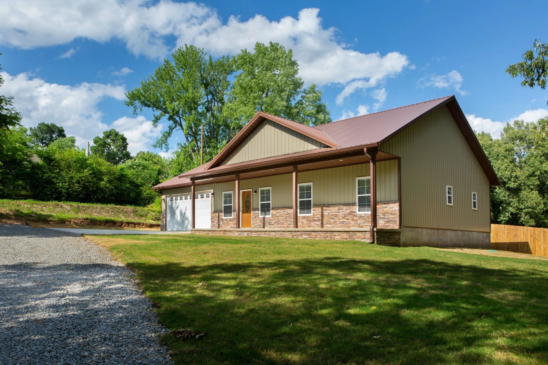 Modern suburban house with stone facade and metal roof under a blue sky.