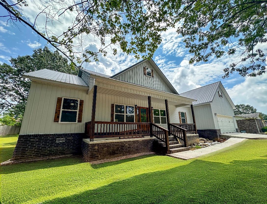 White farmhouse with wooden porch and a spacious green lawn under a bright sky.
