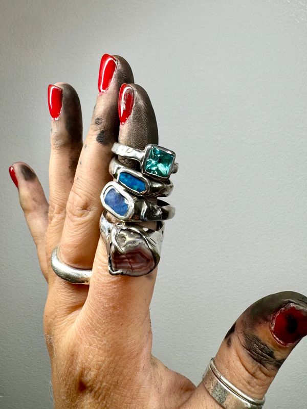 Hand with red nail polish and several silver rings, fingers stained black.