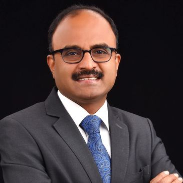 Professional man in suit with glasses and a blue tie against a black background.