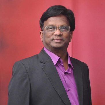 Man in glasses wearing a black blazer and purple shirt against a red background.