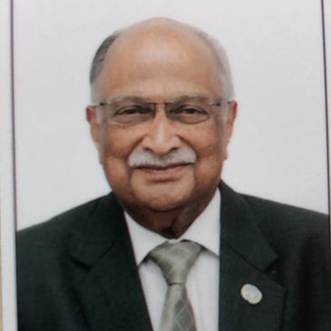 Elderly man in a suit and tie with glasses, smiling.