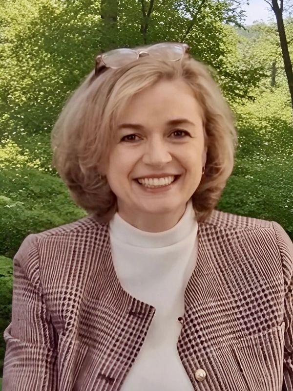 Smiling woman with short blonde hair in a checkered jacket outdoors.