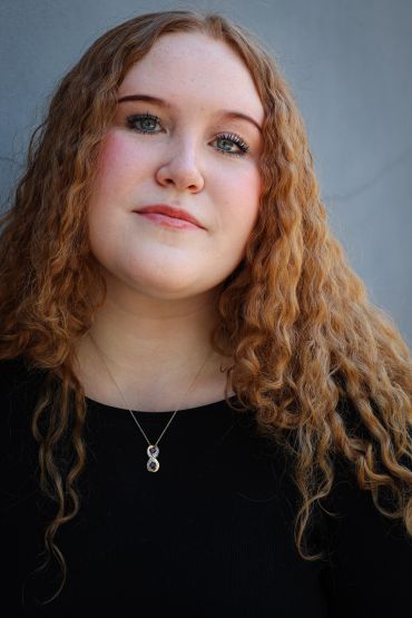 Young woman with curly red hair wearing a black top.