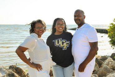 Three people smiling near a waterfront on a sunny day.