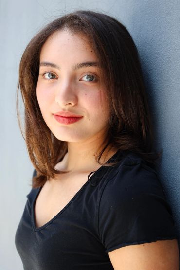 Young woman in black shirt leans against a wall.