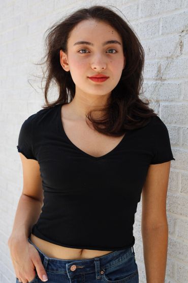 Young woman in a black shirt posing against a white brick wall.