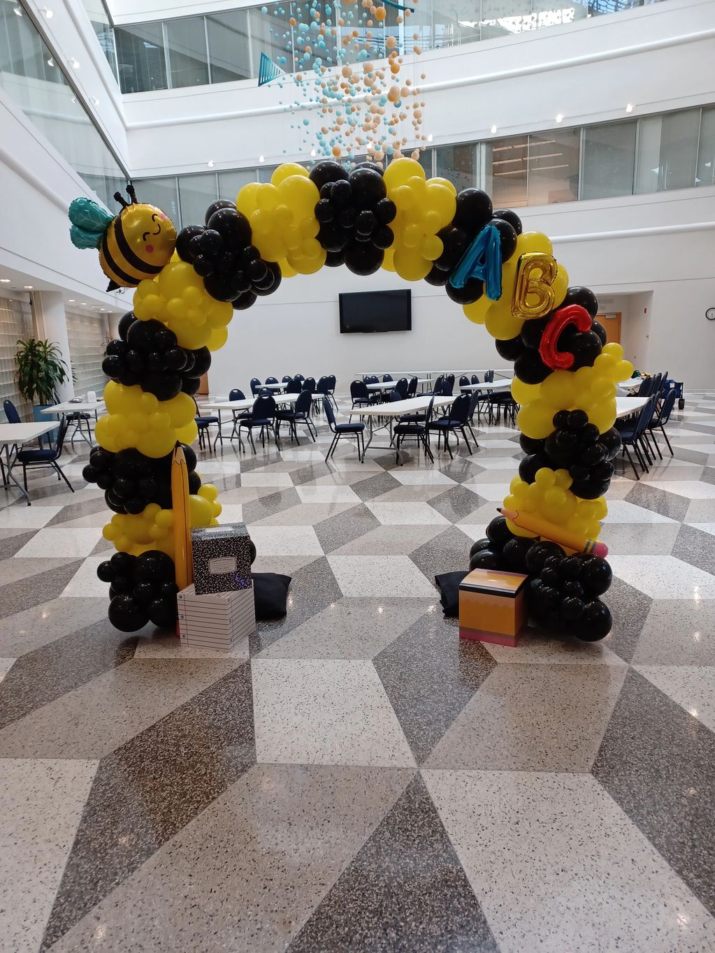 Bee-themed balloon arch with ABC letters and school supplies.