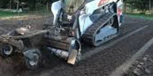 A compact tracked tractor preparing soil in a field under sunlight.