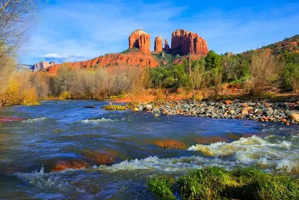 River flowing in front of red rock formations under blue sky.