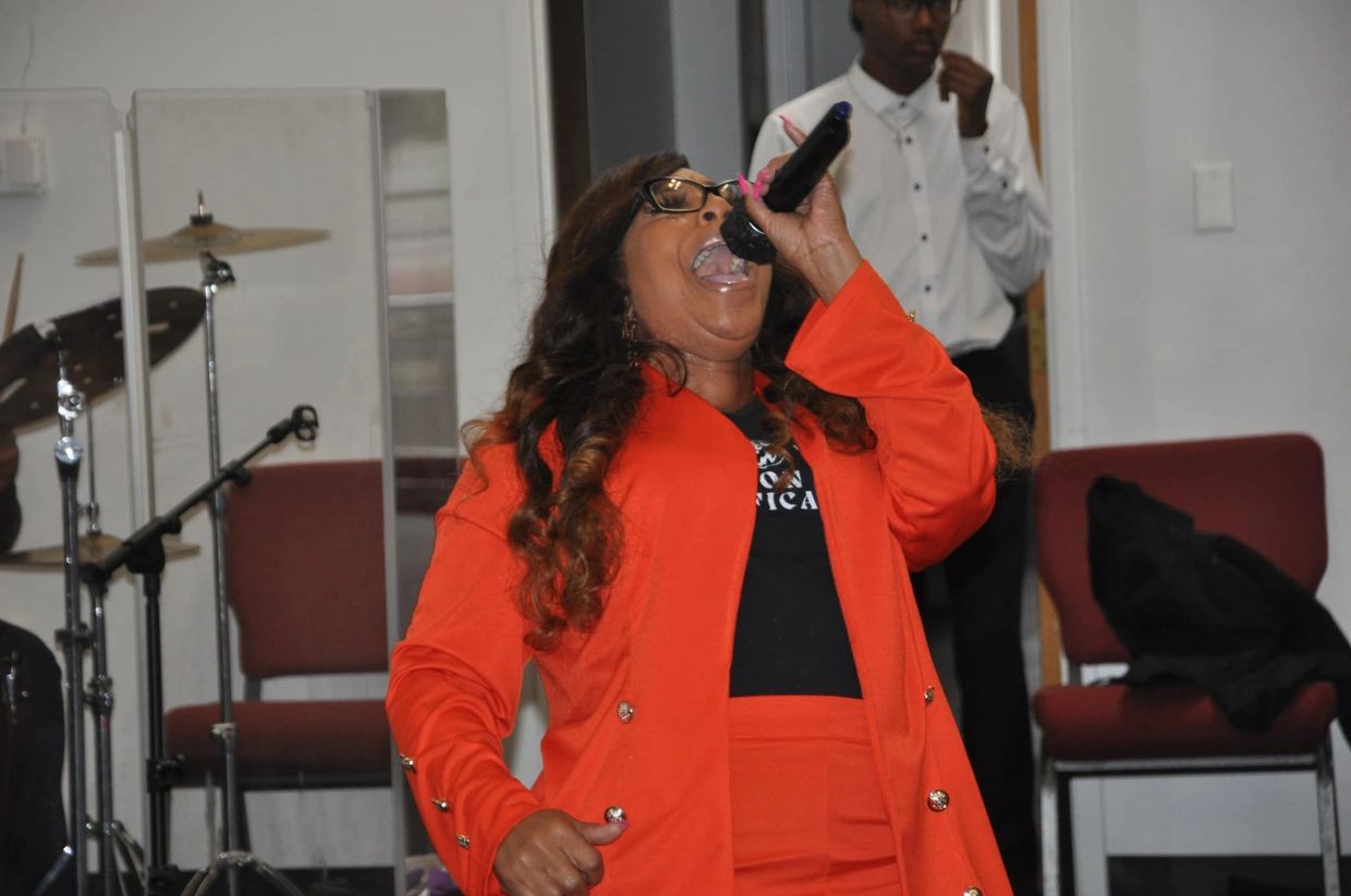 Woman passionately singing into a microphone while wearing an orange suit.