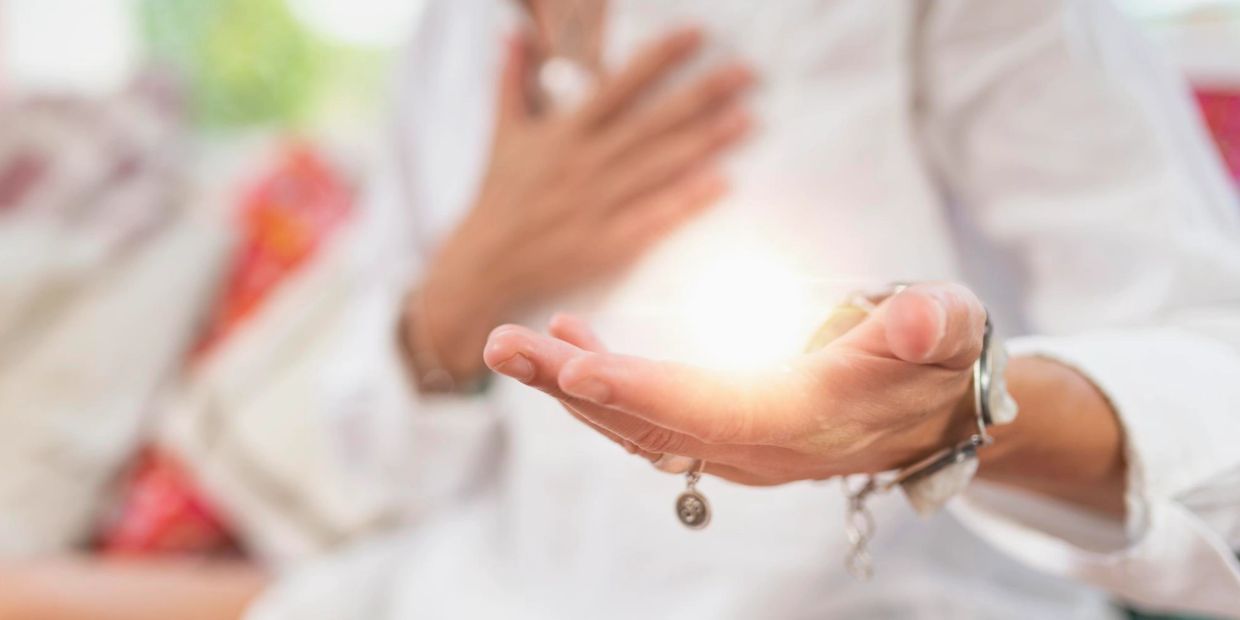 A person holding a glowing light in their hand with the other hand on their chest, symbolizing energy or healing.