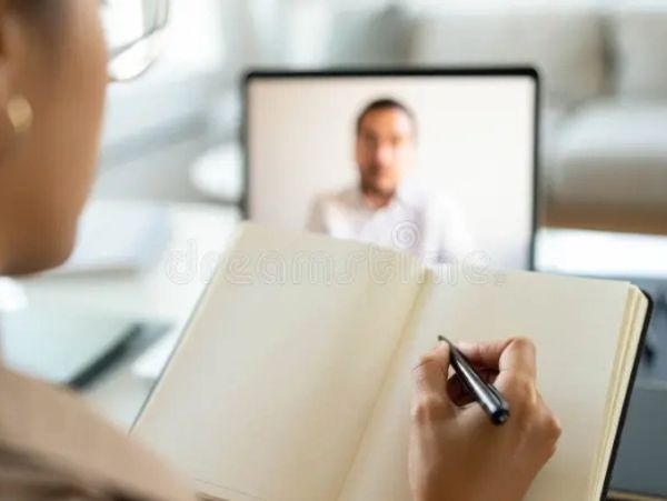 Person taking notes during a video call on a laptop.
