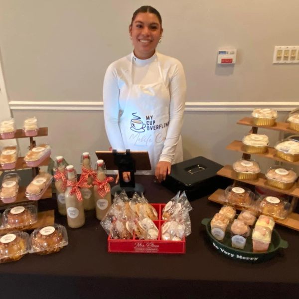 Woman selling baked goods and drinks at a booth with a smile.