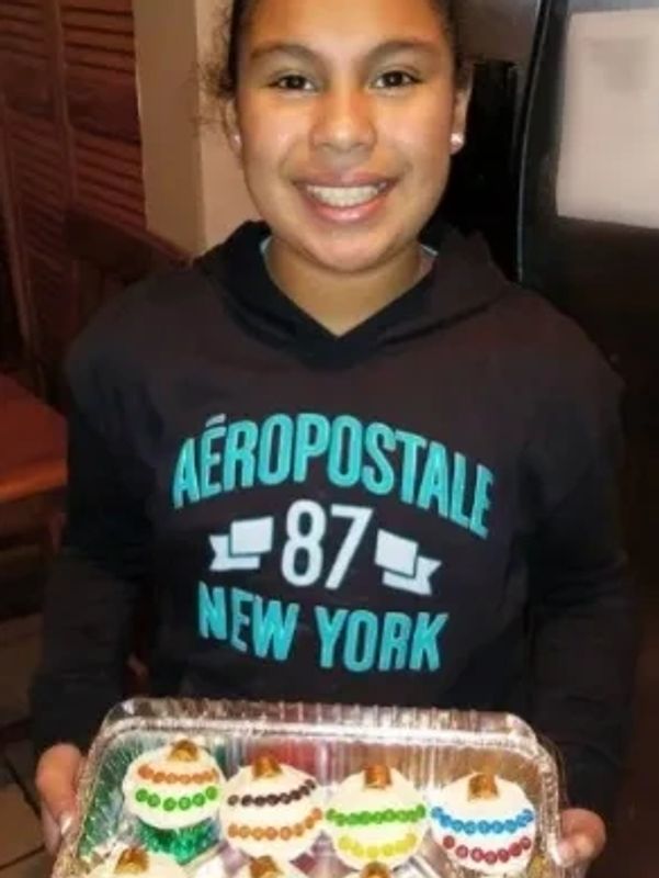 Smiling girl holding a tray of decorated cupcakes.