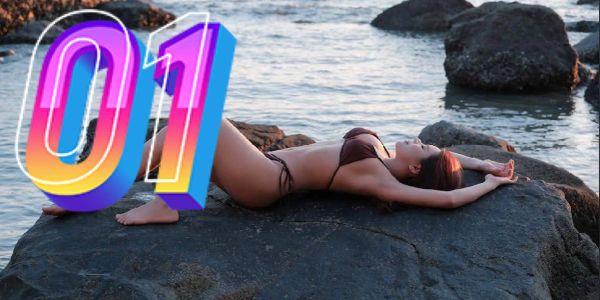 Woman in bikini lying on a rock by the water at sunset.