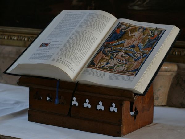 An open religious book with illustrations on a wooden stand.
