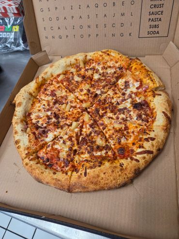 A pineapple and bacon pizza in a cardboard box with a word search game on the lid.