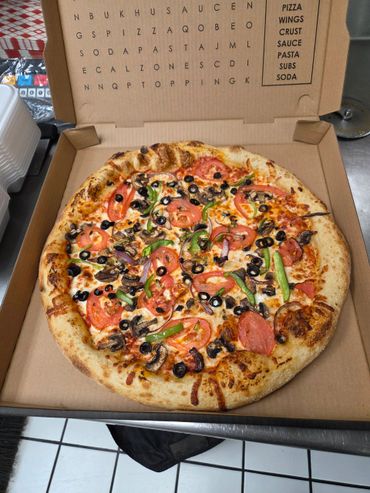 A freshly baked veggie pizza in a cardboard box with a word search on the lid.