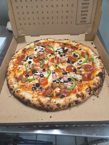 A freshly baked pizza with pepperoni, green peppers, olives, ham, and sausage in a cardboard box.