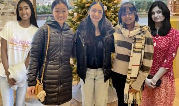 Group of five young women standing together, smiling.