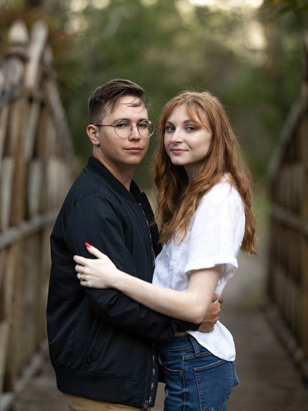 Couple embracing on a wooden bridge, looking at the camera.