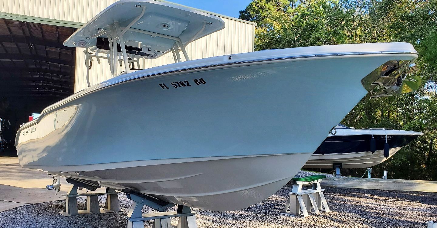 A sleek white boat on stands near a warehouse with trees in the background.