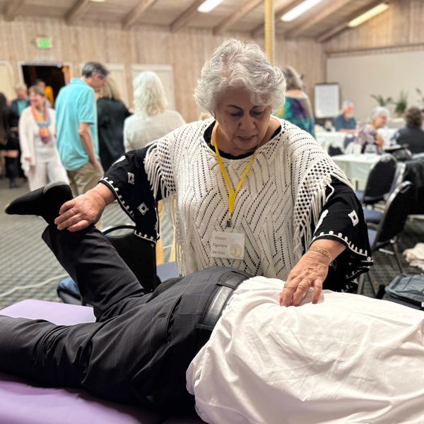 A woman performs a therapeutic stretch on a man lying on a table in a busy room.