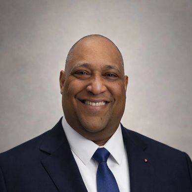 Smiling man in a suit and tie against a neutral background.