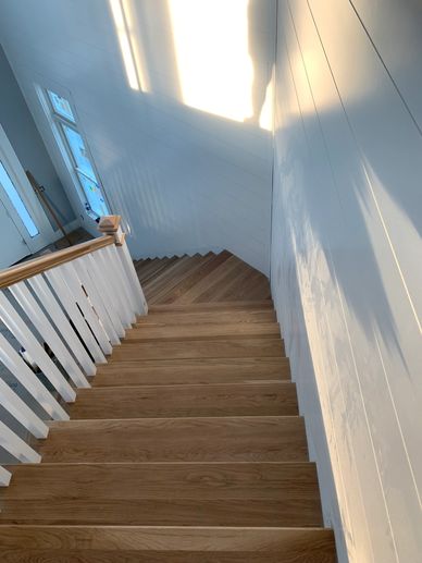 Sunlight casts shadows on a wooden staircase with white railings.