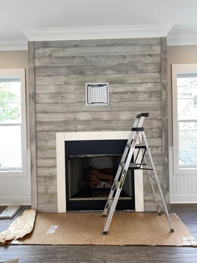 Ladder in front of a wooden-paneled fireplace under renovation.