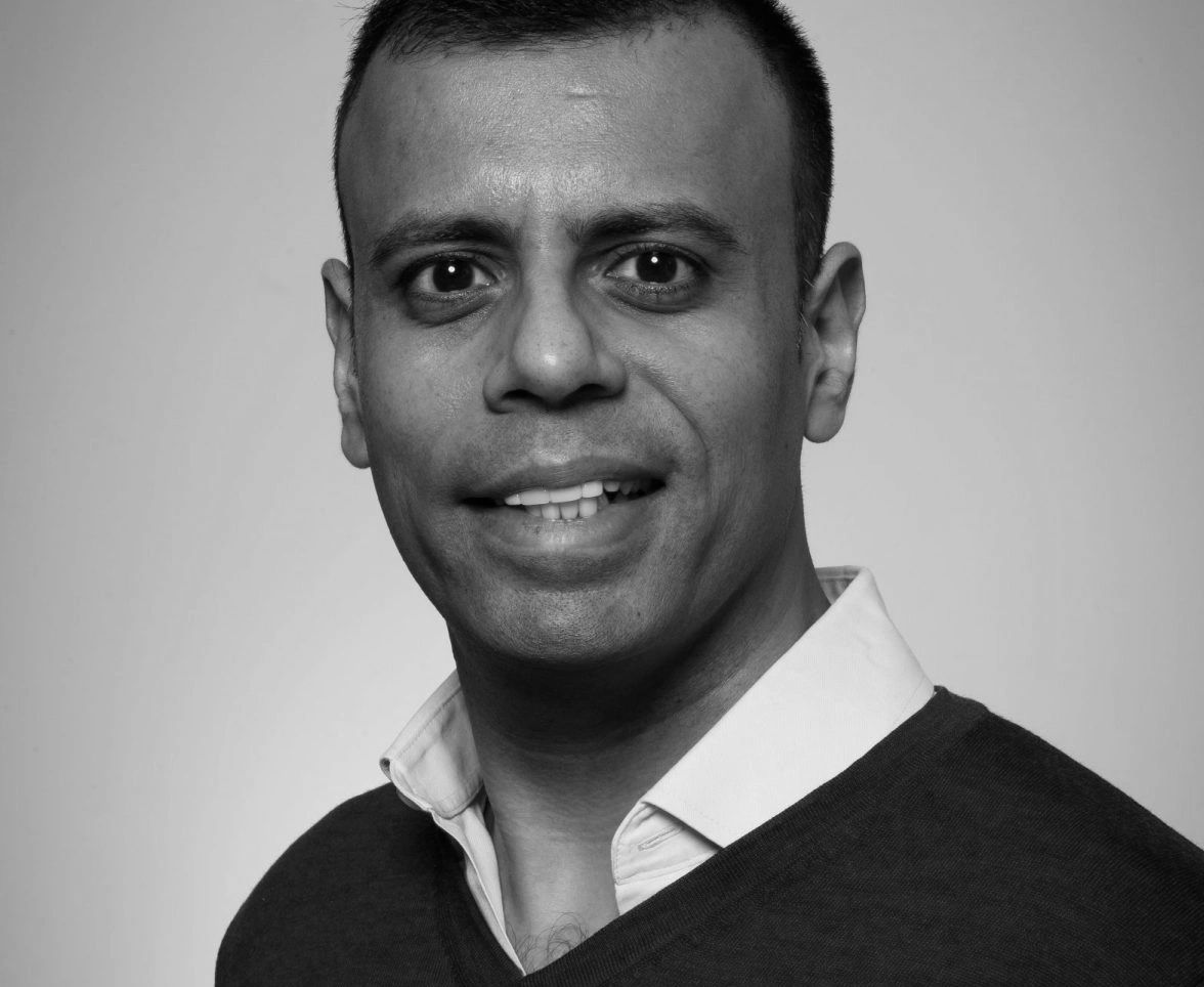 Man with a friendly smile wearing a blue sweater and white shirt.