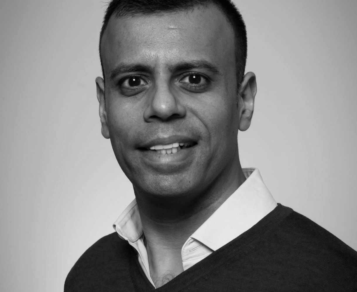 Man with a friendly smile wearing a blue sweater and white shirt.