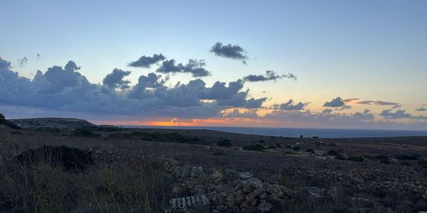 Sunset over a rocky, arid landscape with scattered clouds and distant ocean horizon.