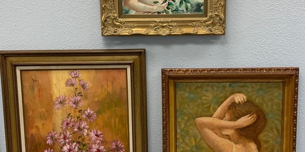 Three framed paintings hanging on a wall, depicting flowers and a woman.