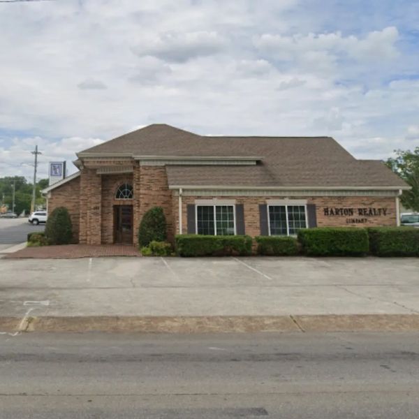 Brick building housing Harton Realty with a large parking area in front.