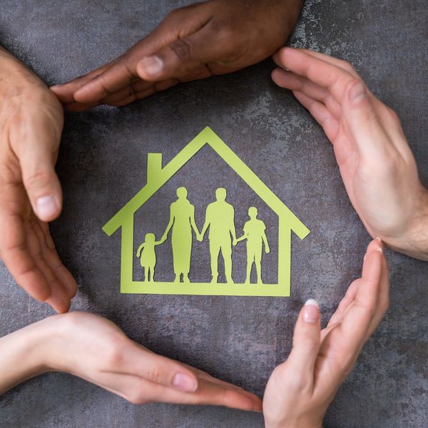 Diverse hands forming a protective circle around a paper cutout of a family in a house.