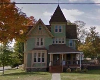 Victorian-style house with a pointed tower and front porch in autumn.