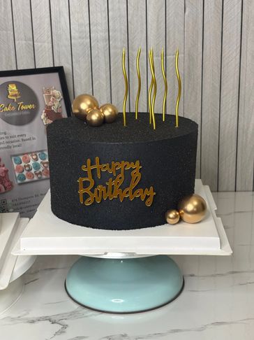 An elegant black birthday cake adorned with sparkling glitter, metallic gold details, and gold balls