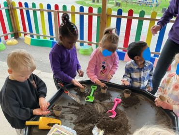 Children playing with soil at a sensory table outdoors.