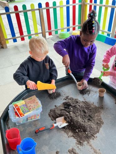 Children playing with soil and gardening tools at a colorful play area.